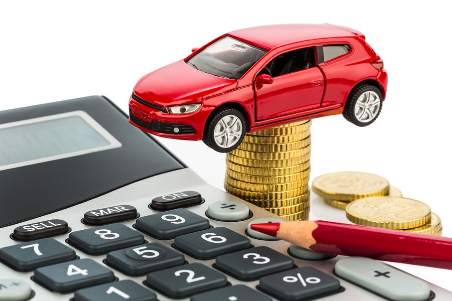 A red car sitting on coins, a calculator, and a red pencil on white background