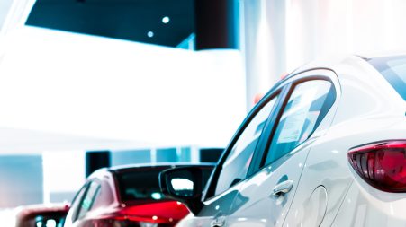 rear-view-of-white-luxury-car-parked-in-modern-showroom-for-sale-white-shiny-car-on-blurred-red-car_t20_1n4Qyg