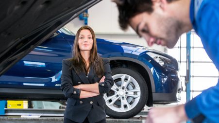Business woman, waiting patiently while a mechanic works under the hood of her car in a garage